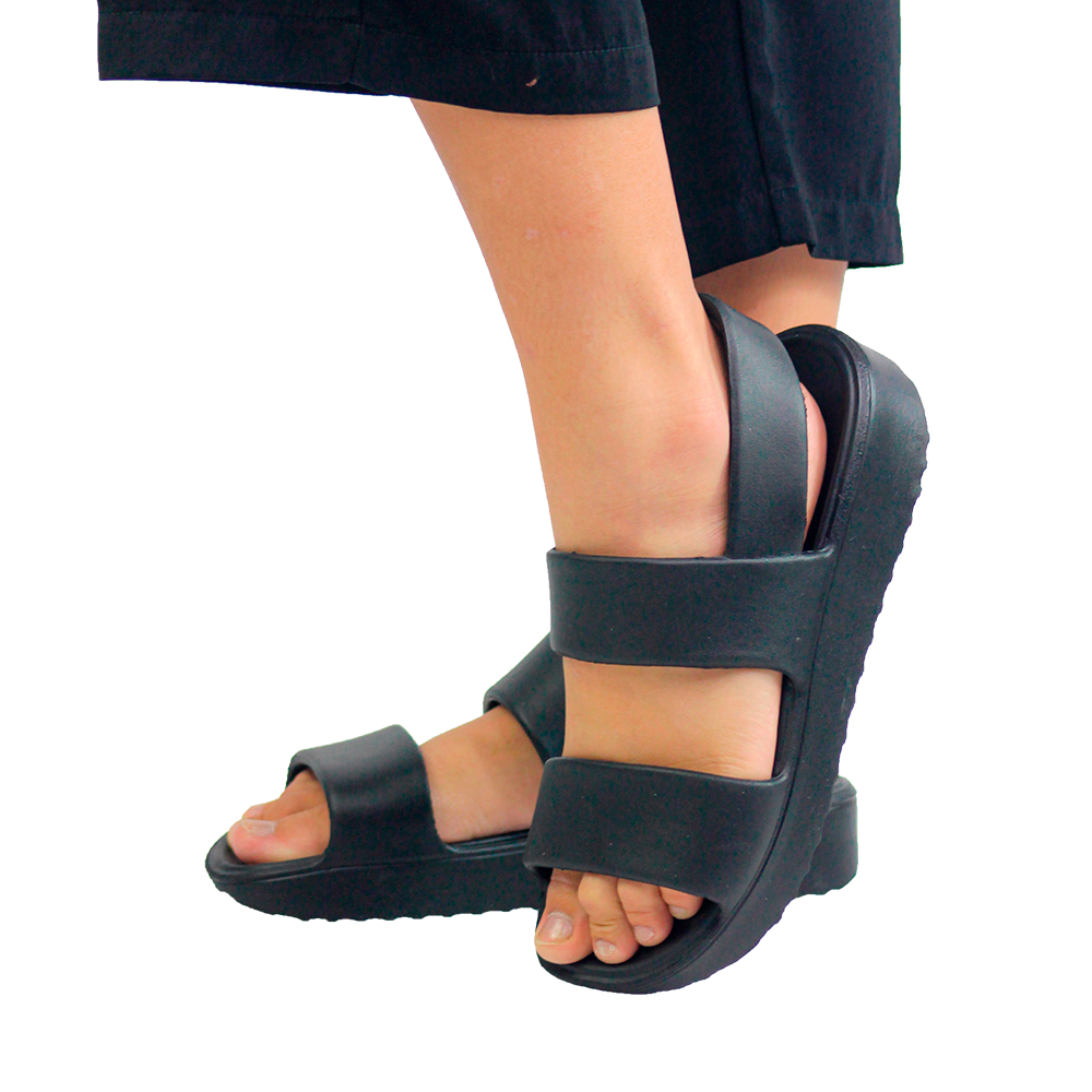 A imagem mostra uma pessoa utilizando a sandália ortopédica Fly Feet classic, com a correia prendendo o calcanhar, na cor preta