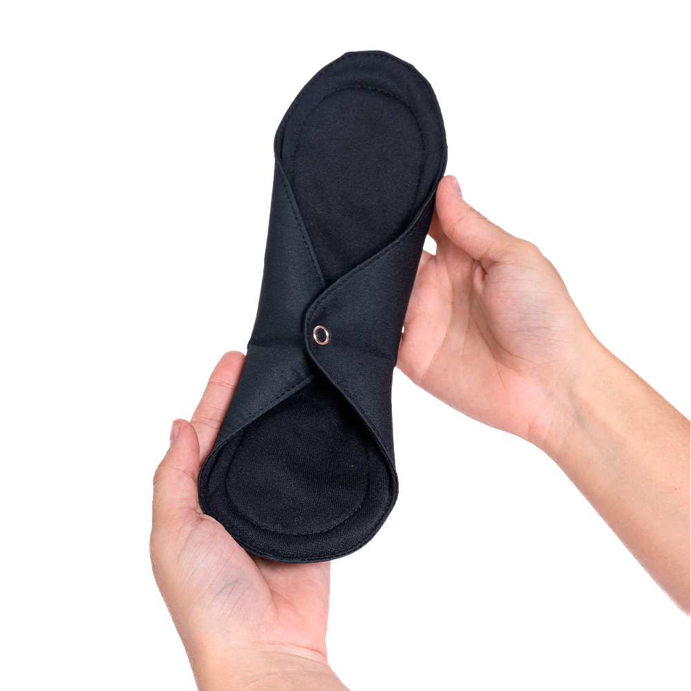 Mãos femininas segurando um absorvente reutilizável com suas abas presas, na cor preto.