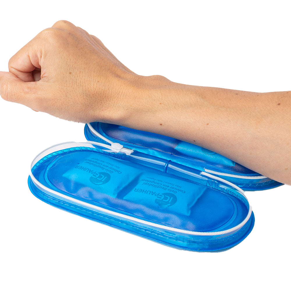 imagem mostra um antebraço apoiado em um estejo térmico aberto apoiado sobre a mesa. Na imagem é possivel ver que o estojo é um azul translúcido e em cada lado dele, contém dois saquinhos de gelo em gel por dentro da estrutura.