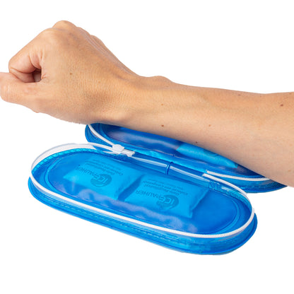 imagem mostra um antebraço apoiado em um estejo térmico aberto apoiado sobre a mesa. Na imagem é possivel ver que o estojo é um azul translúcido e em cada lado dele, contém dois saquinhos de gelo em gel por dentro da estrutura.