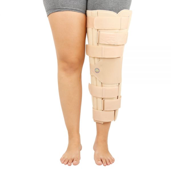 Aimagem mostra a parte dos membros inferiores do corpo, onde a perna esquerda se encontra mobilizada com imobilizador de joelhos fixo na cor bege.