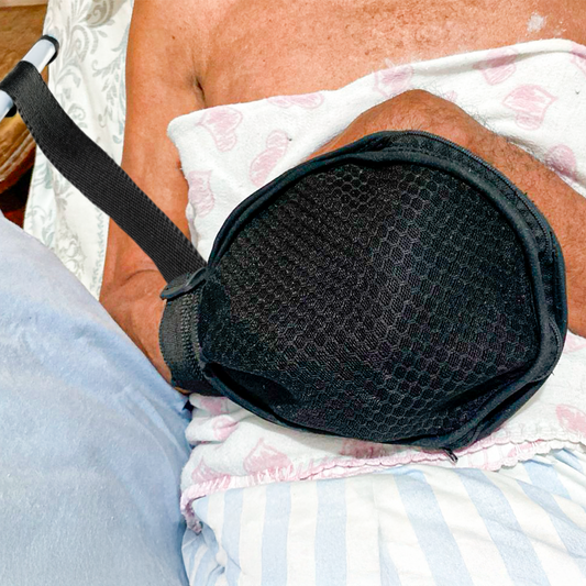 Uma pessoa acamada utilizando a luva de contenção. A luva está presa a maca e na mão direita.