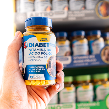 Pessoa segurando o pote de suplemento alimentar em cápsulas, contem 60 cápsulas. Cor do pote: azul e amarelo. 