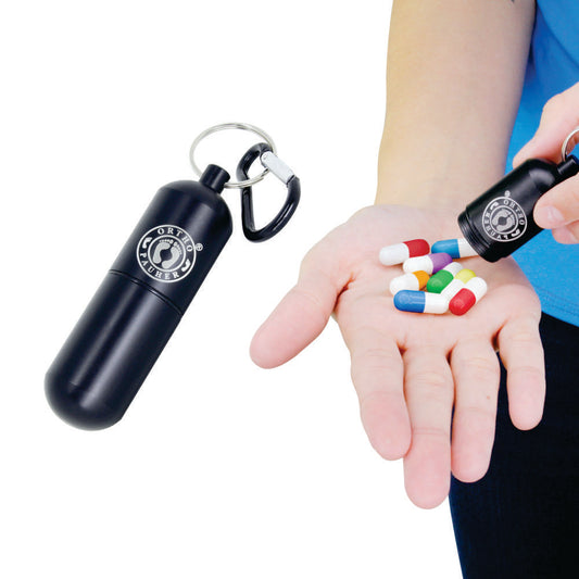 Pessoa tirando capsúla do porta comprimidos, com o produto completo ao lado da pessoa, seu formato é cilindrico de cor preta com a logo da Ortho Pauher na parte superior na cor prata.