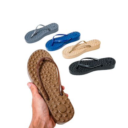 Pessoa segurando sandália Ortopédica Flyfeet Relax, mostrando a superfície com protuberâncias em alto relevo, projetada para ativar a circulação e estimular as terminações nervosas da planta dos pés, promovendo relaxamento e alívio da dor. Cores disponíveis: marrom, azul, preto, grisalho e bege. 