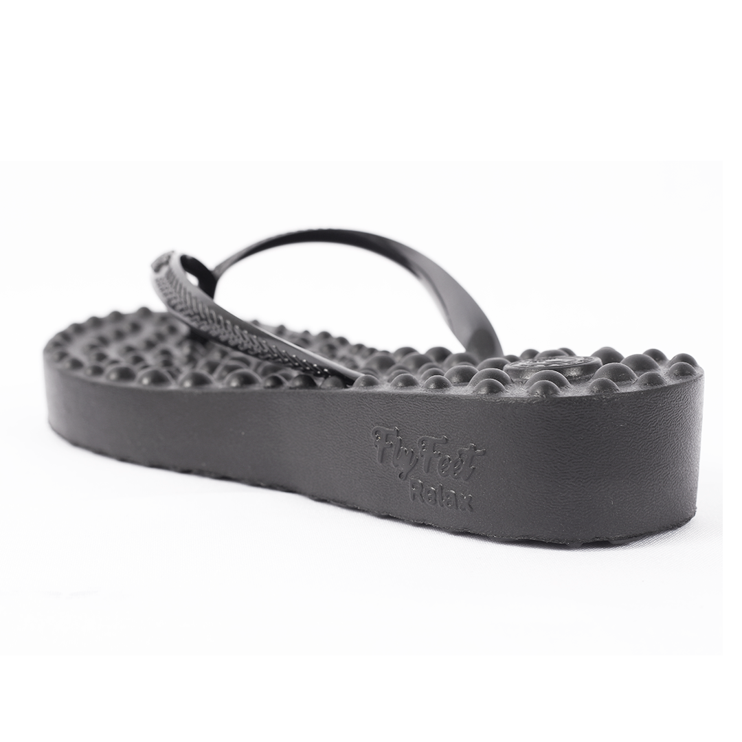 Sandália Ortopédica Flyfeet Relax, cor preta, com destaque para o salto anabela. É possivel ver superfície com protuberâncias em alto relevo, projetada para ativar a circulação e estimular as terminações nervosas da planta dos pés, promovendo relaxamento e alívio da dor.