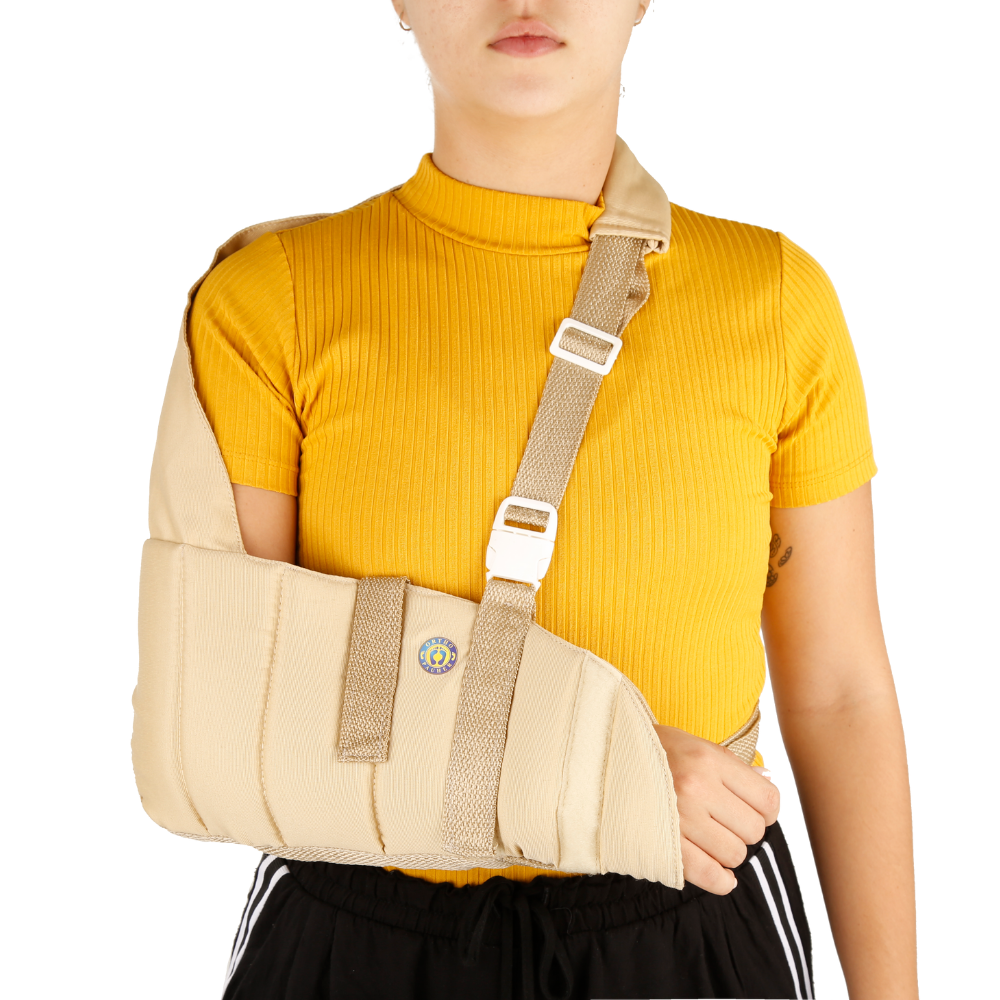 Mulher de frente para a camêra utilizando uma tipoia no braço direito, na cor bege com a logo da Ortho Pauher a parte superior da tipoia