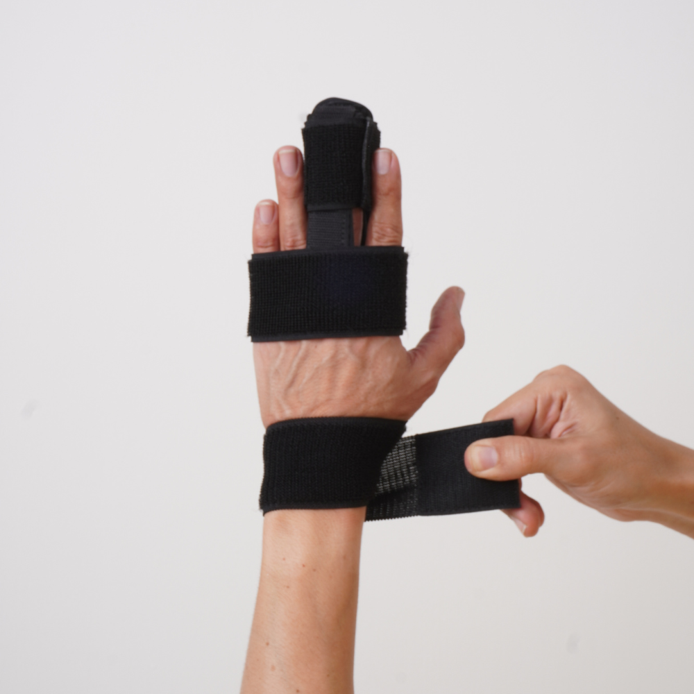 Imagem mostra o braço e a mão esquerda com a tala imobilizadora sendo prendida na area do punho.