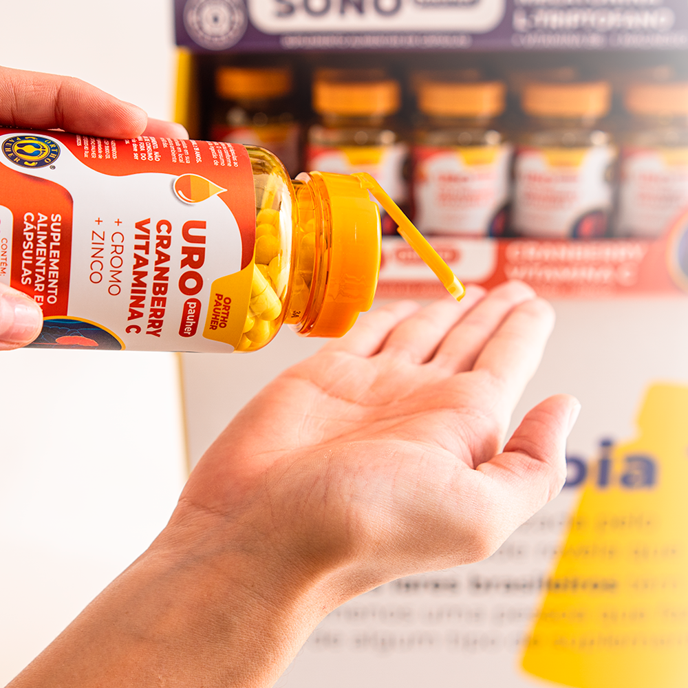 Pessoa segurando pote cheio de capsulas do suplemento alimentar uropauher, cor laranja. 