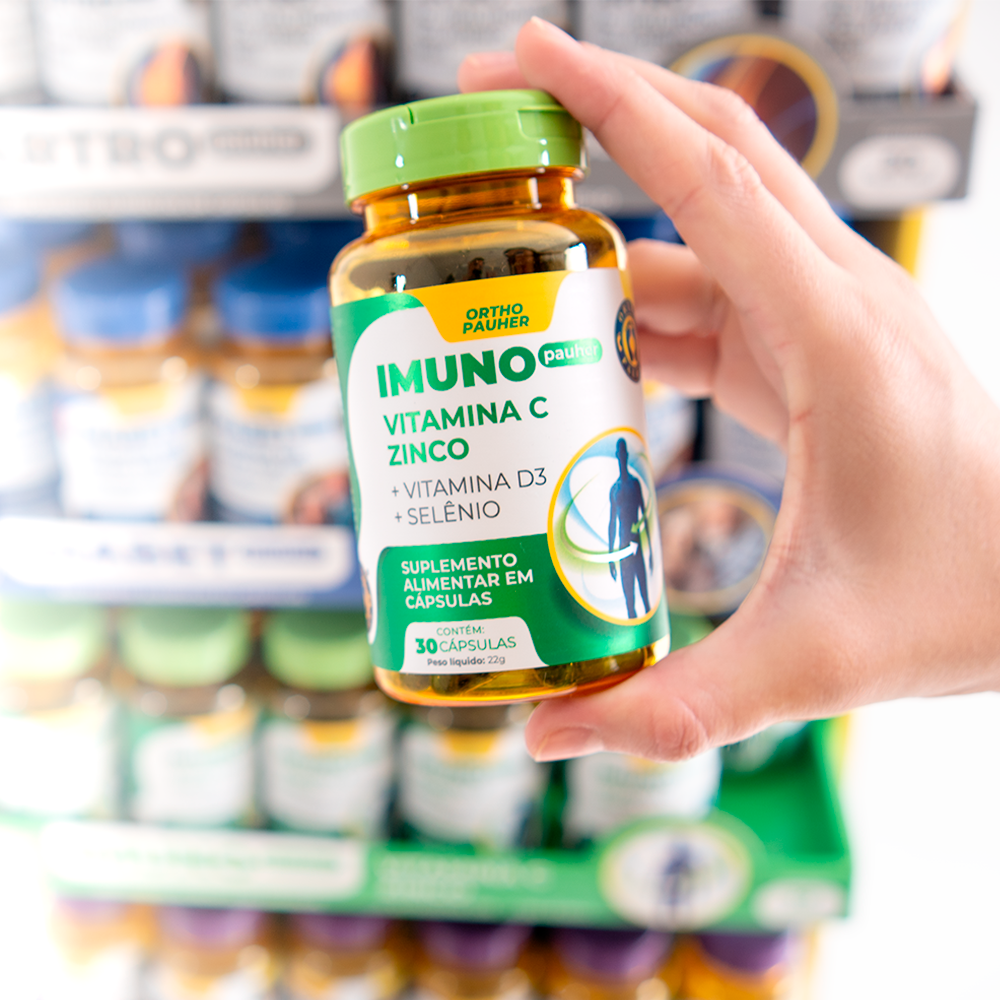 Pessoa segurando suplemento alimentar imuno pauher, com 30 cápsulas.  Cor do pote: verde com amarelo.