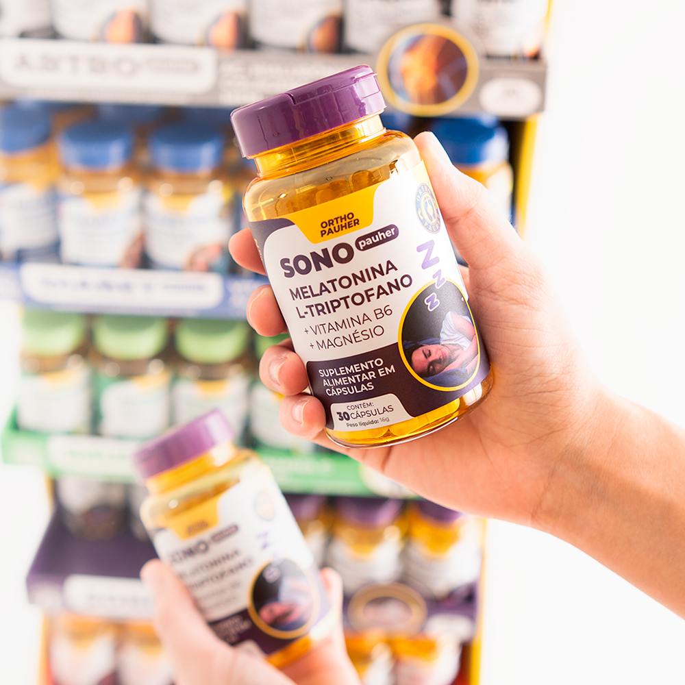 Pessoa segurando pote de suplemento alimentar sono pauher, com 30 cápsulas. Cor do pote roxo e amarelo.